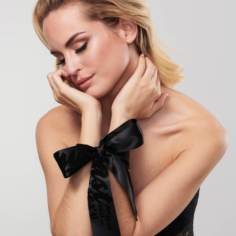 bijoux-indiscrets-silky-sensual-satynowe-szarfy-do-krepowania-czarne-zawiazane-w-kokarde-na-nadgarstkach-pieknej-blondynki