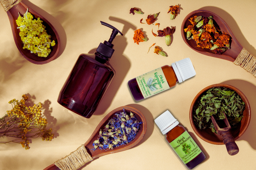 olejki-eteryczne-bamer-naturalne-kaprolowy-herbaciany-w-szklanych-buteleczkach-z-suszonymi-kwiatami-lacznikami-drewnianymi-i-brazowa-butelka-z-pompka-na-bezowym-tle