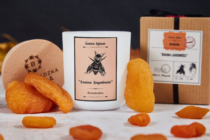 swieca-sojowa-kraina-lagodnosci-brzoskwinia-naturalna-swieczka-z-drewnianym-wieczkiem-w-ekologicznym-opakowaniu-w-otoczeniu-suszonych-brzoskwin