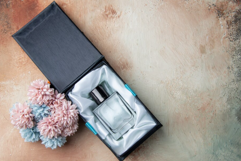 Flakon perfum w eleganckim pudełku, obok pastelowych kwiatów