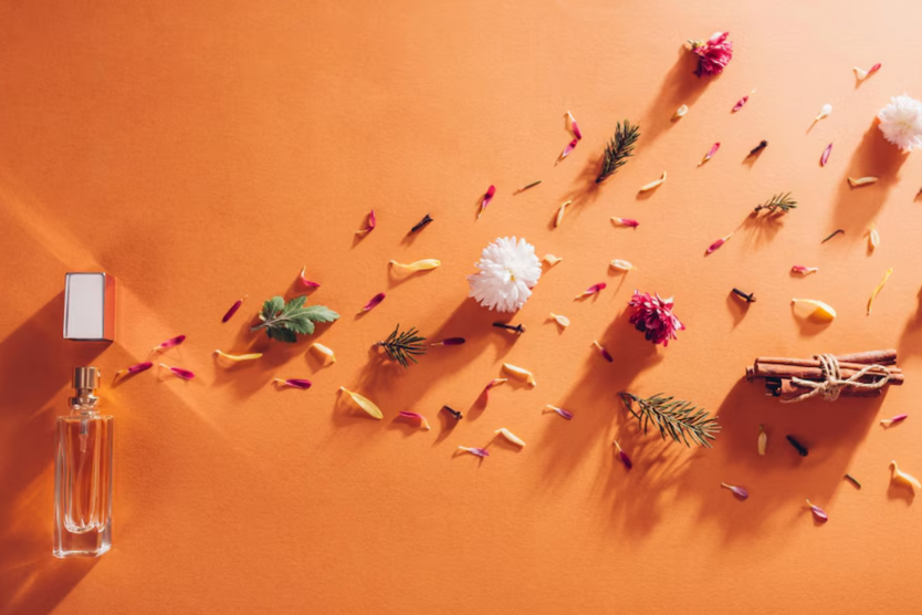 Flakon perfum z przyprawami, kwiatami i listkami na pomarańczowym tle